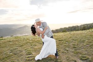 Bride and groom on top of a mountains. The man is dipping the woman. In wedding attire. Photo taken at a Colorado elopement by Michelle Betz Photography