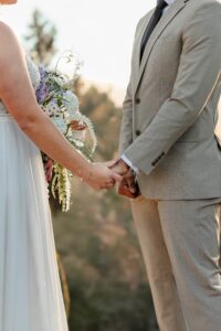 A detail shot of a bride and groom holding hands during the ceremony. Surrounded by Colorado mountains.