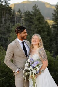 The bride and groom are both smiling, the bride smiling at the camera, the groom smiling at her.