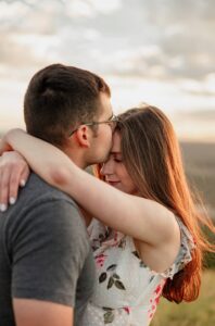 couple posing with kissing her on her forehand. intimate pose with mountain background and golden sunlight. Colorado engagement photographer 