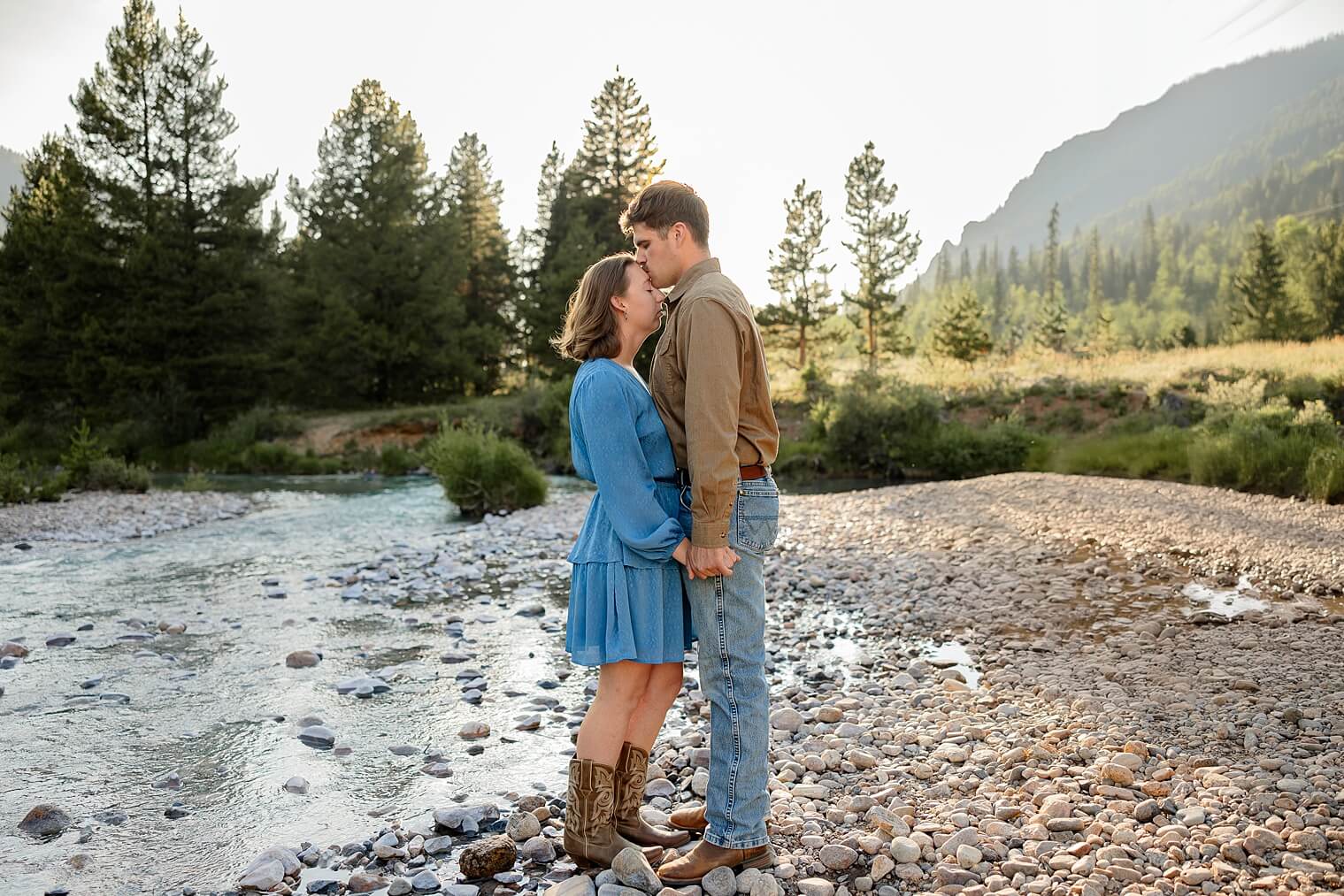 Couple embracing each other holding hands. Surrounded by a creek. mountains, and forest tress.