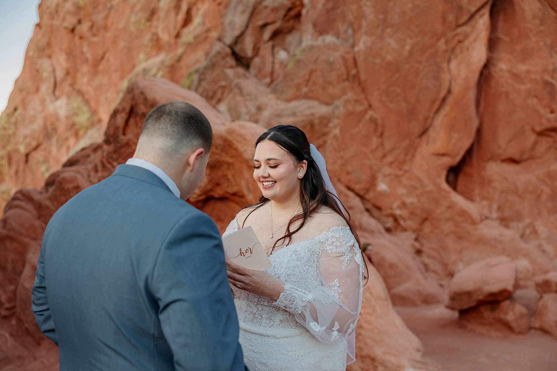 A bride smiling while reading her wedding vows to her soon to be husband. Surrounded by Garden of the Gods red rocks.