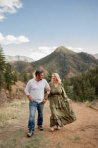 A couple holding hands and smiling at each other. Surrounded by Colorado Springs mountains. Photo taken by a Denver engagement photographer.