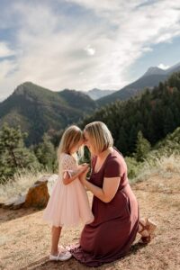 A mother and daughter photo. The mom is kneeling facing her child, they are holding their hands and touching foreheads. Captured by Michelle Betz Photography