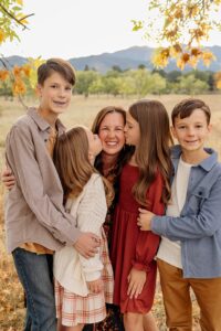 cute photo of children kissing their mother, with some children smiling at the camera. In fall.