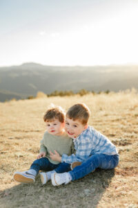 Two toddler brothers sitting down and hugging each other. Surrounded by the Denver Colorado mountains.