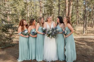 A bride smiling to her bridesmaids. They are all holding their bouquets. Surrounded by the forest at Wedgewood weddings black forest. Captured by Michelle Betz