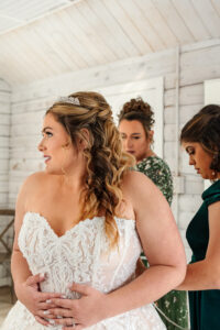 Bride smiling looking away as she gets her dress put on. Located at Pinecrest Event Center