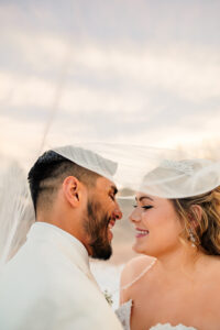 bride and groom portrait, under a vail smiling at each other. Captured by Michelle Betz Photography