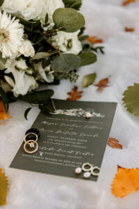 Wedding details image of the invitation, rings, jewelry, and bouquet. Captured by Michelle Betz Photography