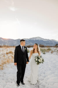 A bride in groom in wedding attire, holding hands and smiling at each other. 