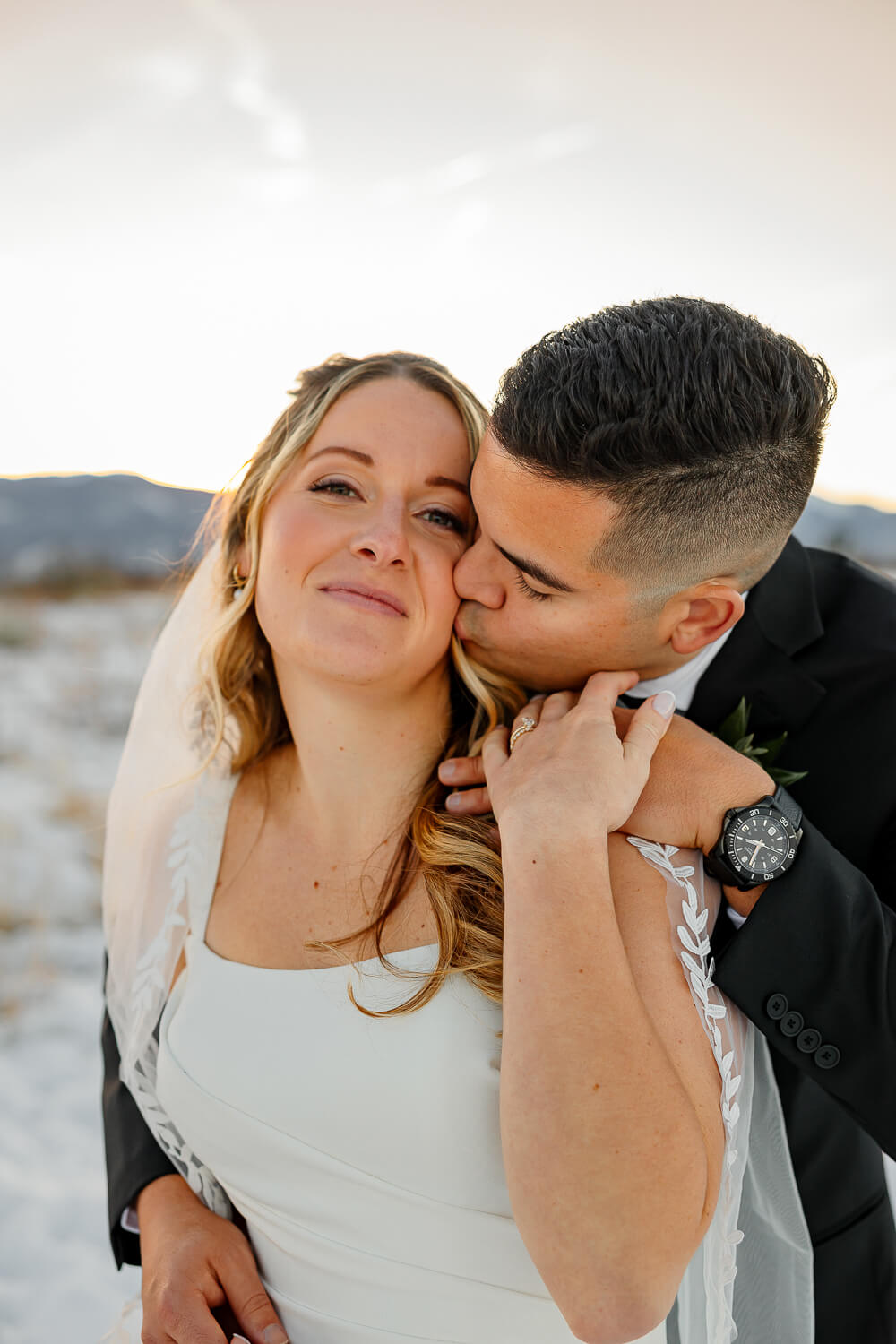 Bride and Groom embracing each other with the groom kissing the bride on her cheek. Surrounded by snow and mountains. Documented by Colorado Springs Wedding Photographer, Michelle Betz Photography