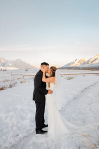 A bride and groom portrait. The brides hands are holding the grooms face. He is kissing her forheard. Surrounded by the Colorado mountains and snow.