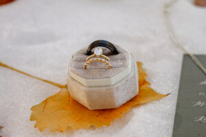 A detail photo of wedding rings. The ring box is on top of a yellow leaf in the snow.