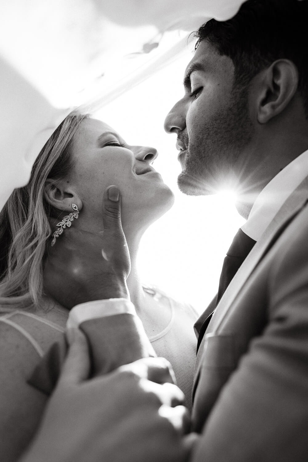 A black and white photo of a bride and groom under a vail. The sun is peaking through. Captured by Colorado wedding photographer, Michelle