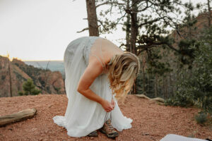 A bride bending over to tie her shoes before she gets married. Surrounded by Colorado Springs mountains. Captured by Colroado wedding. and engagement photographer, Michelle Betz.