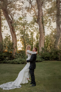 A bride and groom portrait. He is picking her up and they are smiling at each other. Photo taken at a Fort Collins wedding venue.