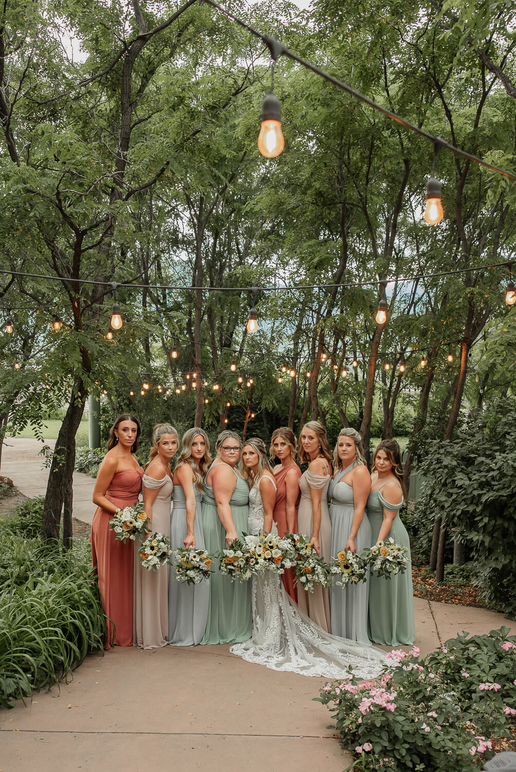 A bridal party portrait. The bride is in the middle surrounded by her bridesmaids. They are holding flowers, and surrounded by gardens. At Hillside Gardens and event center.