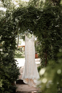 Photo of a wedding dress hanging on a greenery filled arch. Photo captured by Colorado wedding photographer, Michelle Betz