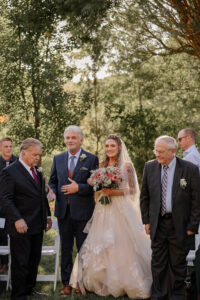 A bride walking down the isle with her father. Surrounded by beautiful Colorado green grass and trees.