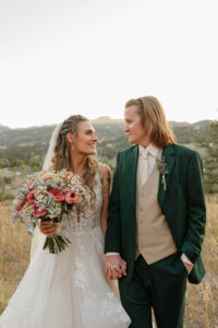 A bride and groom portrait. They are walking and holding hands. Looking at each other, smiling. Photo captured by Michelle Betz Photography.