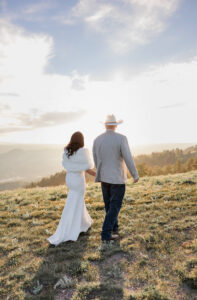 Bride and groom holding hands and walking into the sunshine. Surrounded by Rocky mountains in Colorado.