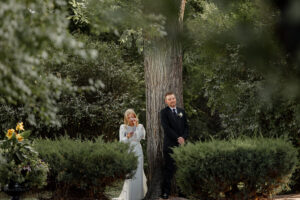 A bride and groom having a first touch. They are on either side of a big tree. The bride is reading her vows privately to the groom. Captured at an affordable Colorado wedding venue. 