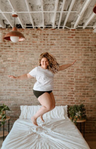 A picture of a women jumping on the bed and smiling. Captured by Michelle Betz Photography