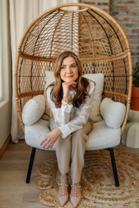 A women smirking to the side, with her chin on her hand. Inside an egg shaped chair. At Kindle Studio in Colorado Springs. 