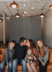 Family sitting on a leather couch inside Kindle studio, mom and dad are kissing.