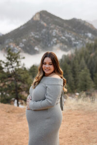 A photo of a pregnant women with her hand on her stomach, smiling down. Surrounded by mountains. Captured by Michelle Betz Photography