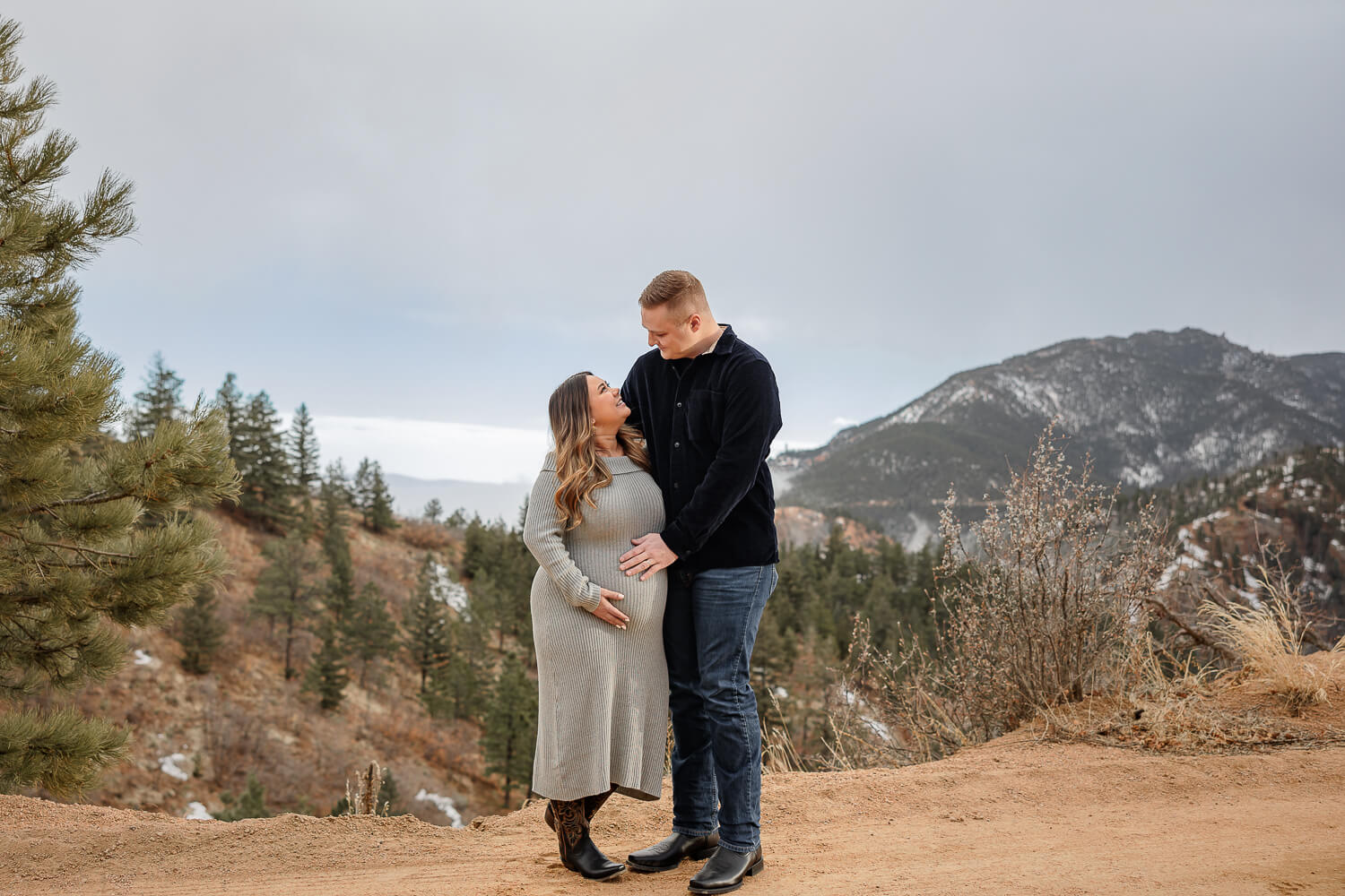 A couple posing for a maternity photoshoot in colorado springs. Their hands are on her pregant stomach, as they look at each other.