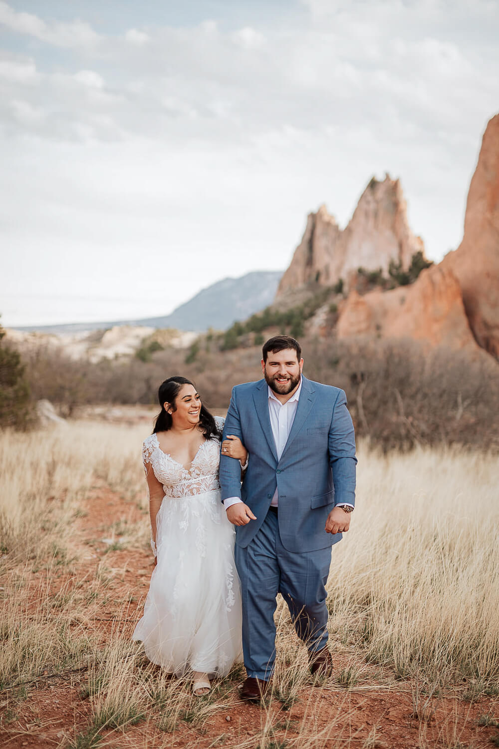 A bride and groom linking arms, walking, and smiling together. Captured by a Colorado wedding photographer.