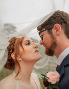 Bride and groom portrait on their wedding day. They are underneath the vail and looking at each other. 