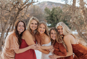 A bride and her bridesmaids smiling and hugging her bridesmaids for a portrait. At a Estes Park Wedding Venue.