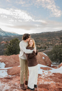 A couple with the manss arms wrapped around her hugging her. He is kissing her temple. Captured by Michelle Betz Photography