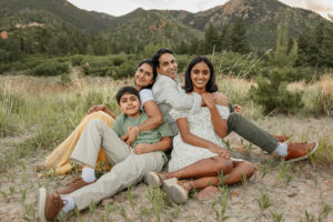 A family portrait with the parents and two older kids. They are sitting on the ground, smiling at the camera. Captured by Colorado Springs family photographer, Michelle Betz