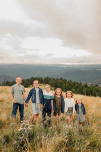 A family photoshoot with 6 kids holding hands. They are smiling at the camera. Surrounded by Colorado Springs mountains. 