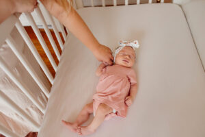 A newborn baby girl in her crib. Her mother is holding her hand.