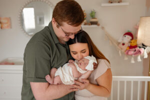 A couple holding their newborn baby girl, looking at the baby together. They are in the nursery. Captured by Professional Newborn photographer, Michelle Betz.