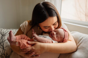 A mother kissing her newborn baby in her home. Captured by Michelle Betz Photography, a Colorado Springs newborn photographer.