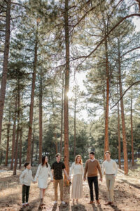 A family holding hands and smiling at the camera in the forest of Fox Run Park in Colorado Springs. Captured by Michelle Betz Photography