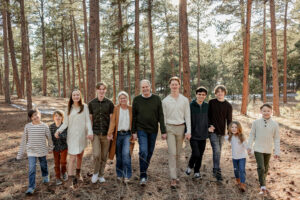 Grandparents and all their grandchildren famil y photo. They are holding hands and walking. Surrounded by forest. Captured by Michelle, a Colorado Springs family photographer.